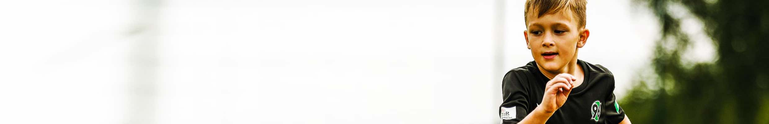 Brandbuilding für Fußballschule 96 Talents + Friends. Leistungen: Name, Logo, Animation, Designtoolbox, Icondesign, Fahrzeugbeschriftung, „Bandenwerbung“ im Fußball-Videospiel FIFA (jetzt: EA Sports FC). Bild: Ein Junge im schwarzen Fußballtrikot von Hannover 96 läuft konzentriert und dynamisch über den Platz.